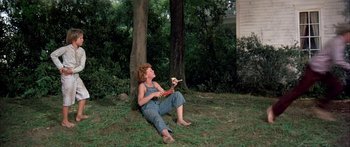 Movie still from “Tom Sawyer” (1973), directed by Don Taylor – A woman sitting on the ground in a yard; Wide shot, High angle