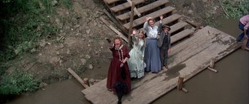 Movie still from “Tom Sawyer” (1973), directed by Don Taylor – A group of people standing next to each other on a bridge; Wide shot, Overhead angle