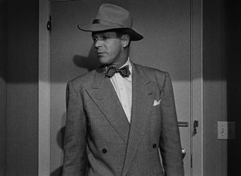 Movie still from “Too Late for Tears” (1949), directed by Byron Haskin – A black and white photo of a man wearing a suit and hat; Medium shot, Low angle
