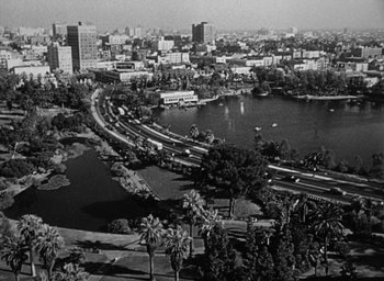 Movie still from “Too Late for Tears” (1949), directed by Byron Haskin – A black and white photo of a lake and a city; Extreme Wide shot, High angle