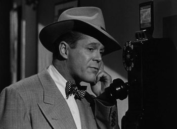 Movie still from “Too Late for Tears” (1949), directed by Byron Haskin – A man wearing a suit and a hat talking on a phone; Close Up shot, Low angle