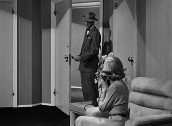 Movie still from “Too Late for Tears” (1949), directed by Byron Haskin – A man in a suit standing in front of a woman in front of a mirror; Wide shot, Over the shoulder angle