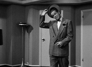 Movie still from “Too Late for Tears” (1949), directed by Byron Haskin – A black and white photo of a man in a suit and hat; Medium shot, Low angle