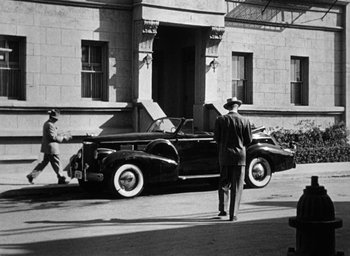 Movie still from “Too Late for Tears” (1949), directed by Byron Haskin – An old car parked in front of a building with people walking by; Wide shot, Low angle