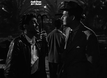 Movie still from “Too Late for Tears” (1949), directed by Byron Haskin – A man holding an umbrella talking to another man; Medium shot, Over the shoulder angle
