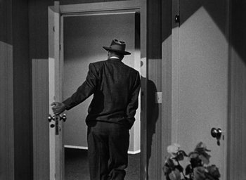 Movie still from “Too Late for Tears” (1949), directed by Byron Haskin – A black and white photo of a man in a suit and a hat; Wide shot, Over the shoulder angle