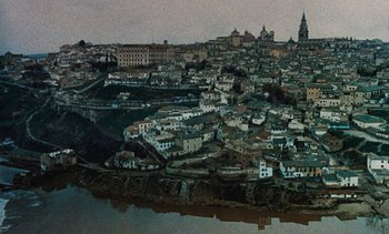 Movie still from “Tristana” (1970), directed by Luis Buñuel – An aerial view of a city with a body of water in front of it; Extreme Wide shot, High angle