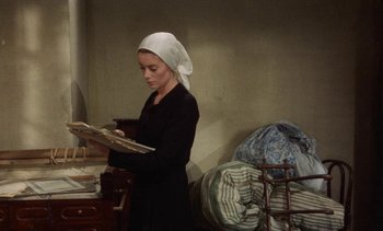 Movie still from “Tristana” (1970), directed by Luis Buñuel – A woman standing in a room holding a painting; Medium shot, High angle