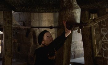 Movie still from “Tristana” (1970), directed by Luis Buñuel – A woman in black shirt holding onto a brown object; Medium shot, Overhead angle