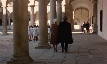 Movie still from “Tristana” (1970), directed by Luis Buñuel – A man and a woman walking through an archway; Extreme Wide shot, High angle