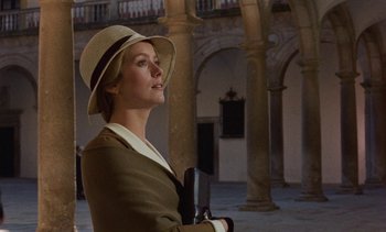 Movie still from “Tristana” (1970), directed by Luis Buñuel – A woman wearing a hat and holding a book in her hands; Medium shot, Low angle