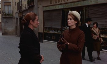 Movie still from “Tristana” (1970), directed by Luis Buñuel – Two women standing on the sidewalk talking to each other; Medium shot, Over the shoulder angle