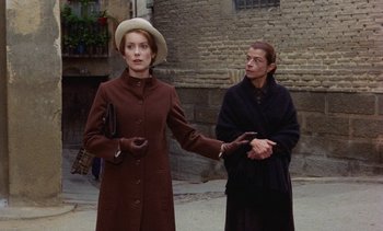 Movie still from “Tristana” (1970), directed by Luis Buñuel – A woman in a brown coat and a man in a black coat; Medium shot, Over the shoulder angle