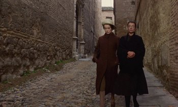 Movie still from “Tristana” (1970), directed by Luis Buñuel – A man and a woman walking down a stone path; Wide shot, High angle