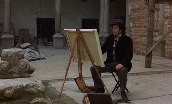 Movie still from “Tristana” (1970), directed by Luis Buñuel – A man sitting in front of an easel painting; Wide shot, High angle