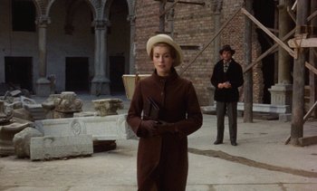 Movie still from “Tristana” (1970), directed by Luis Buñuel – A woman in a brown coat holding an umbrella in front of a man in a brown suit; Medium shot, Low angle