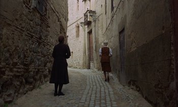 Movie still from “Tristana” (1970), directed by Luis Buñuel – Two women are walking down an alley way; Extreme Wide shot, High angle
