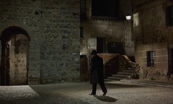 Movie still from “Tristana” (1970), directed by Luis Buñuel – A man in a black coat walking in the dark; Extreme Wide shot, High angle