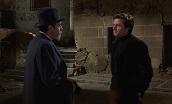Movie still from “Tristana” (1970), directed by Luis Buñuel – A man in a top hat talking to another man in a black suit; Medium shot, Over the shoulder angle