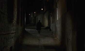 Movie still from “Tristana” (1970), directed by Luis Buñuel – A person walking down a dark alley way at night; Wide shot, High angle