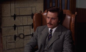 Movie still from “Tristana” (1970), directed by Luis Buñuel – A man in a suit and tie sitting in a chair; Close Up shot, High angle