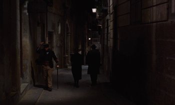 Movie still from “Tristana” (1970), directed by Luis Buñuel – A group of people walking down a street at night; Wide shot, High angle