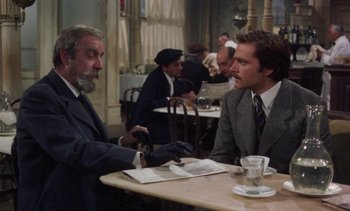 Movie still from “Tristana” (1970), directed by Luis Buñuel – Two men sitting at a table in front of each other at a restaurant; Medium shot, Over the shoulder angle