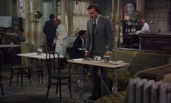 Movie still from “Tristana” (1970), directed by Luis Buñuel – A man in a suit and tie standing at a table in a restaurant; Wide shot, High angle