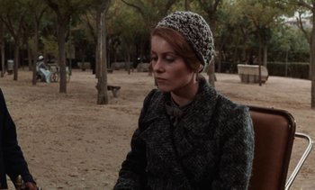 Movie still from “Tristana” (1970), directed by Luis Buñuel – A woman sitting in the sand wearing a hat; Medium shot, Over the shoulder angle