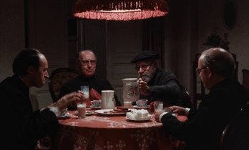 Movie still from “Tristana” (1970), directed by Luis Buñuel – A group of people sitting around a table eating; Medium shot, High angle