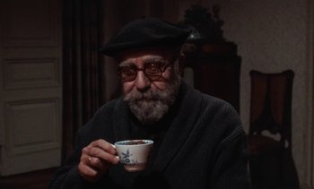 Movie still from “Tristana” (1970), directed by Luis Buñuel – An old man with a beard and glasses holding a coffee cup; Medium shot, High angle