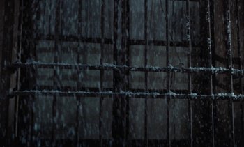 Movie still from “Tristana” (1970), directed by Luis Buñuel – A rain covered fence in a dark room; Wide shot, Low angle