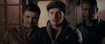 Movie still from “Wild Bill” (2011), directed by Dexter Fletcher – A man wearing a hat and a brown jacket; Close Up shot, Over the shoulder angle