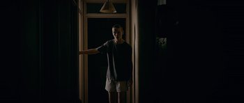 Movie still from “Wild Bill” (2011), directed by Dexter Fletcher – A man standing in a dark room holding his hand out; Medium shot, High angle