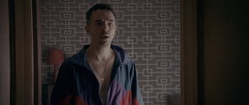 Movie still from “Wild Bill” (2011), directed by Dexter Fletcher – A man with a cross on his chest standing in front of a wall; Close Up shot, Over the shoulder angle