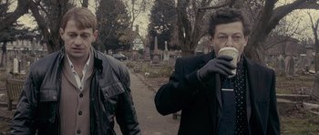 Movie still from “Wild Bill” (2011), directed by Dexter Fletcher – Two men walking down the street in a cemetery; Medium shot, Over the shoulder angle