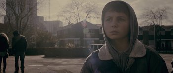 Movie still from “Wild Bill” (2011), directed by Dexter Fletcher – A young boy is standing on the side of the street; Close Up shot, Over the shoulder angle