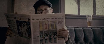 Movie still from “Wild Bill” (2011), directed by Dexter Fletcher – An older man reading a newspaper with a lot of bottles on it; Close Up shot, Low angle