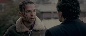 Movie still from “Wild Bill” (2011), directed by Dexter Fletcher – A man in a shearling jacket with a bloody face; Close Up shot, Over the shoulder angle