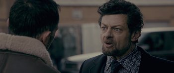 Movie still from “Wild Bill” (2011), directed by Dexter Fletcher – A man with a beard and a suit and tie; Close Up shot, Over the shoulder angle