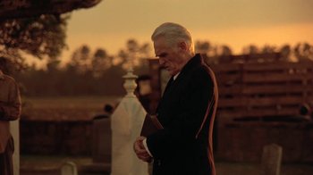 Movie still from “Wild Hearts Can't Be Broken” (1991), directed by Steve Miner – An older man in a black suit is holding a book; Medium shot, Low angle