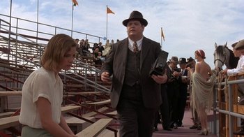 Movie still from “Wild Hearts Can't Be Broken” (1991), directed by Steve Miner – A man in a suit and hat walking in front of a crowd of people; Medium shot, Low angle