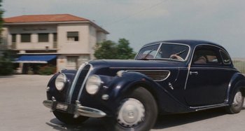 Movie still from “Your Vice Is a Locked Room and Only I Have the Key” (1972), directed by Sergio Martino – An old fashioned car driving down a street; Wide shot, Low angle