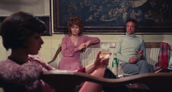 Movie still from “Your Vice Is a Locked Room and Only I Have the Key” (1972), directed by Sergio Martino – A woman sitting in front of two other people in front of a painting; Medium shot, Over the shoulder angle