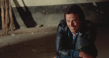 Movie still from “Your Vice Is a Locked Room and Only I Have the Key” (1972), directed by Sergio Martino – A man sitting on the ground smiling for the camera; Close Up shot, High angle