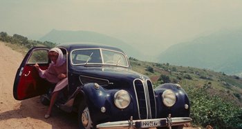 Movie still from “Your Vice Is a Locked Room and Only I Have the Key” (1972), directed by Sergio Martino – An old fashioned car parked on the side of a road; Wide shot, High angle