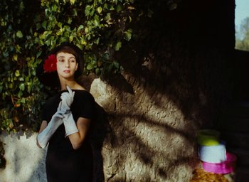 Movie still from “Ô saisons ô chateaux” (1958), directed by Agnès Varda – A woman in a black dress standing next to a tree; Medium shot, Low angle