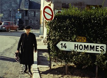 Movie still from “Ô saisons ô chateaux” (1958), directed by Agnès Varda – An old woman walking down the street with a dog; Wide shot, High angle