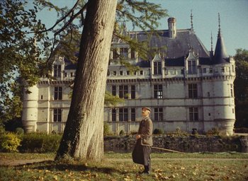 Movie still from “Ô saisons ô chateaux” (1958), directed by Agnès Varda – A man standing next to a tree in front of an old building; Extreme Wide shot, Low angle