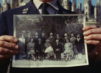 Movie still from “Ô saisons ô chateaux” (1958), directed by Agnès Varda – A man holding an old photo of a family; Medium shot, Overhead angle
